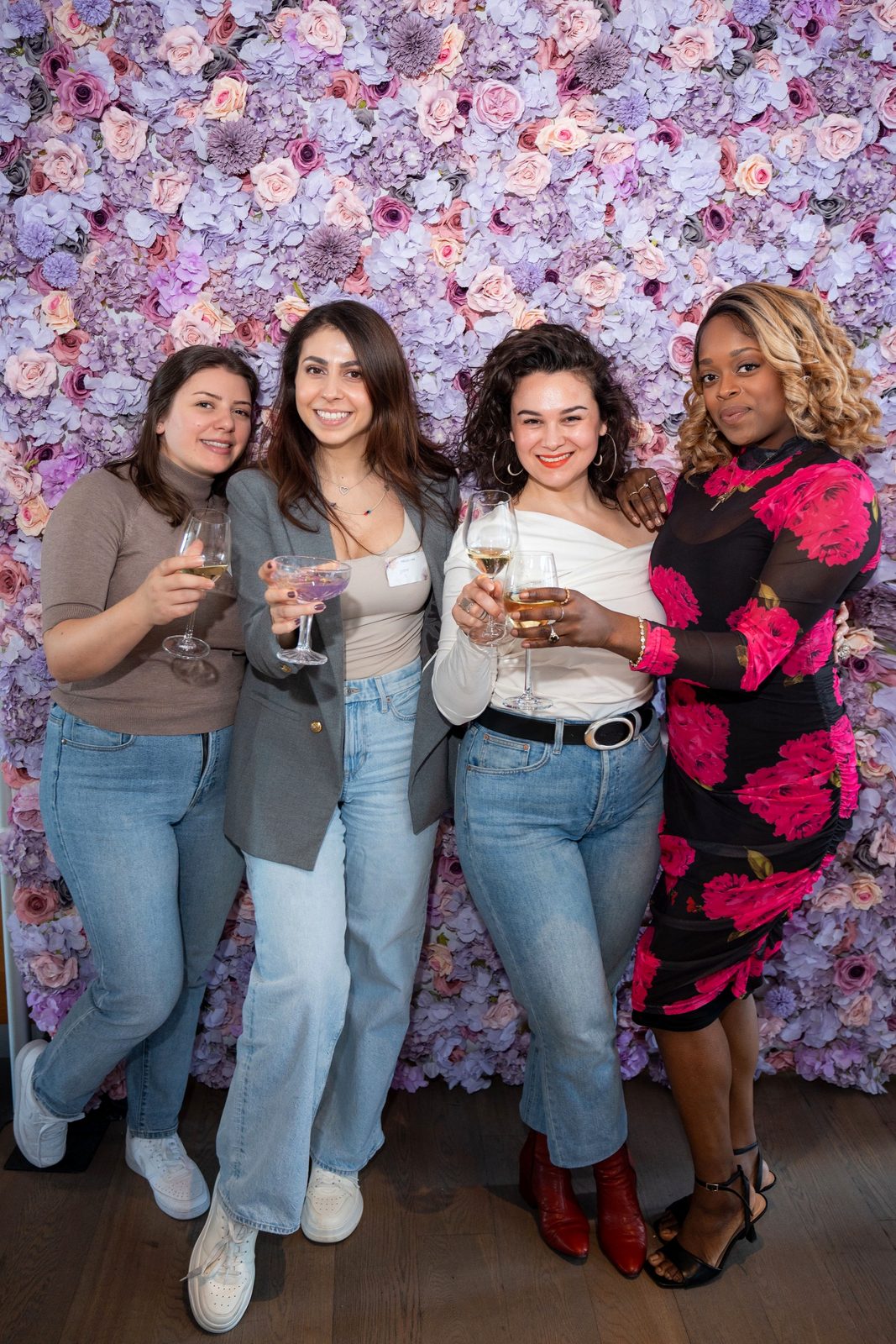 Four women toasting together in front of the flower wall