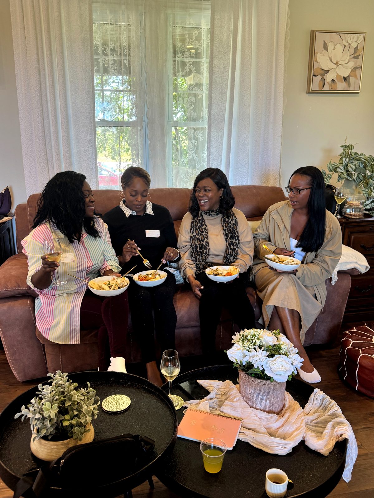 Women laughing together over bowls of food on the couch