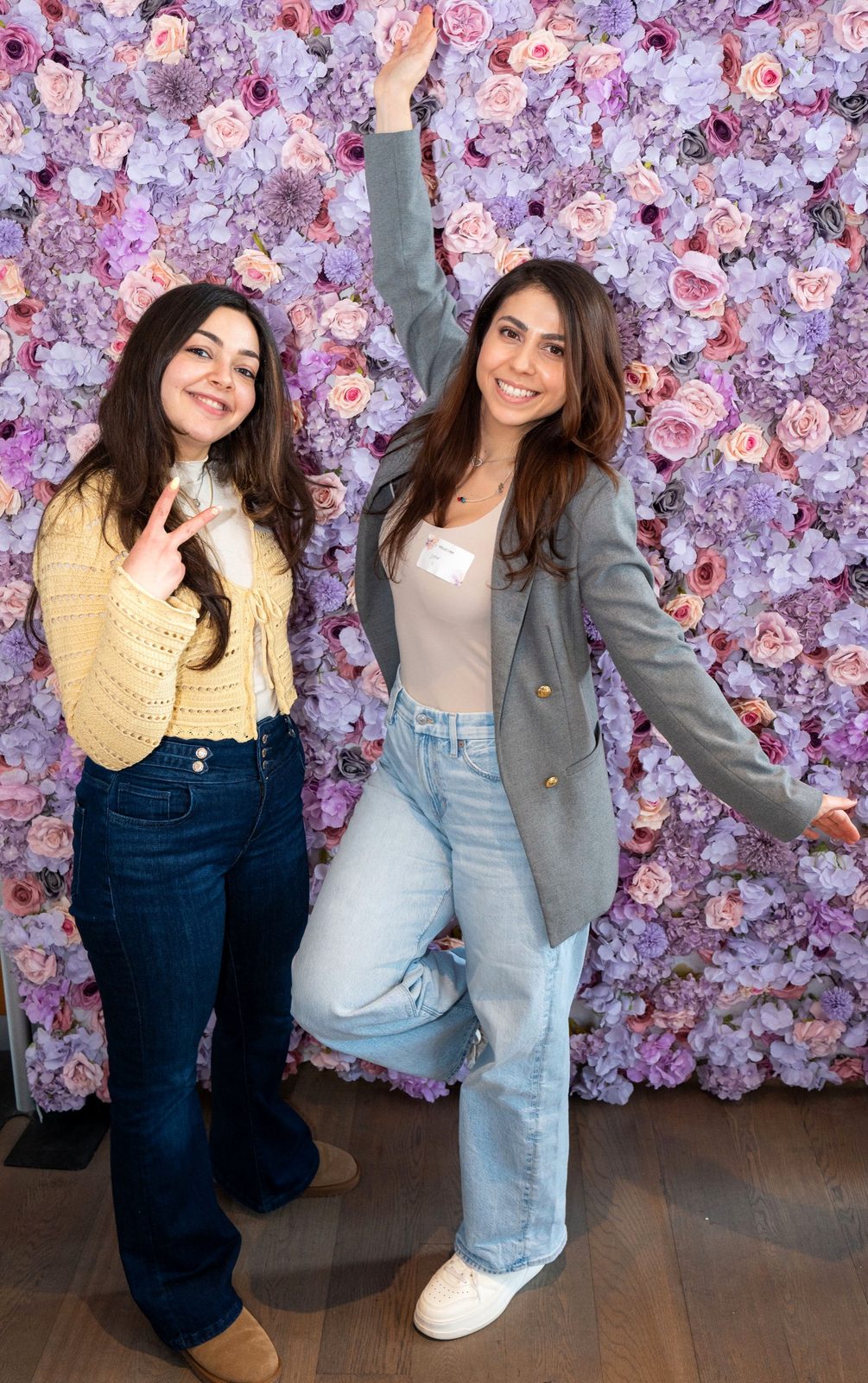 Two women striking a playful pose in front of the flower wall
